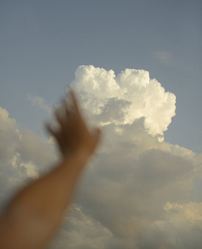 A hand reaching toward a sunlit cloud